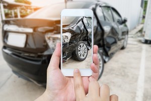 hands holding a smartphone to photograph a damaged car