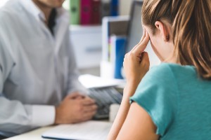 young woman with head pain talking to doctor