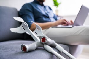 young man with crutches and laptop on sofa