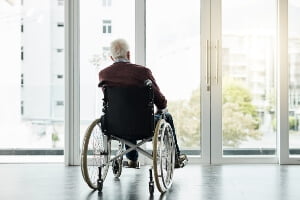 Elderly man sitting in wheelchair facing window.
