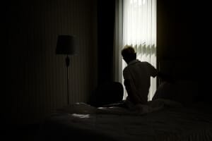 A man sitting on a bed alone in a dark room.